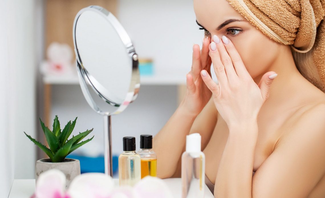 Młoda kobieta nakłada kosmetyki do pielęgnacji twarzy na swoją twarz.
