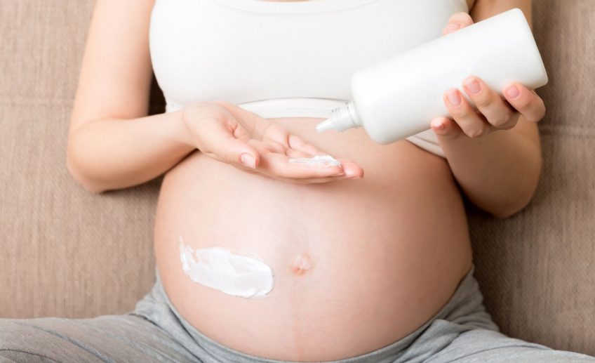 KObieta stosuje kosmetyki w ciąży, aby pozbyć się rozstępów na brzuchu.