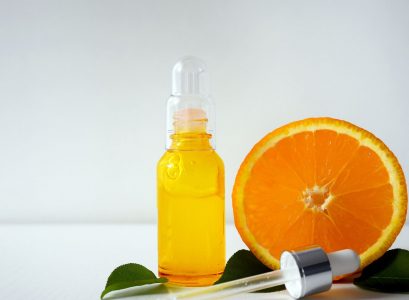 Serum z witaminą C w butelce, a obok niego owoc pomarańczy.