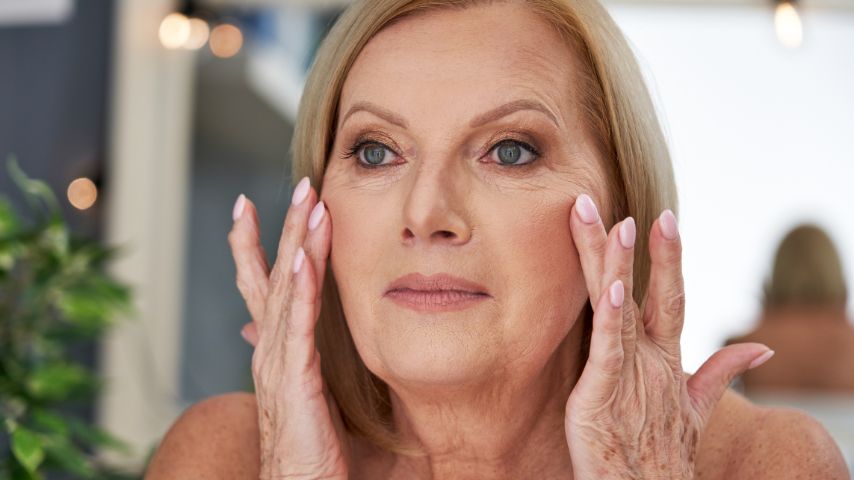 Starsza kobieta sprawdza skórę na twarzy, aby skontrolować, jak działają jej kosmetyki dla seniorów.